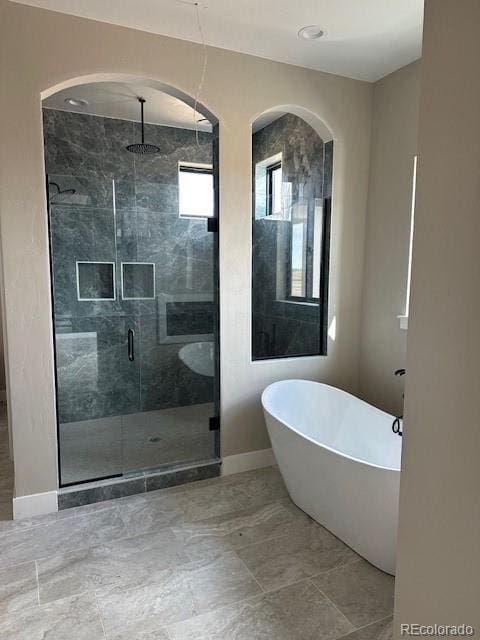 full bathroom featuring marble finish floor, a stall shower, a freestanding tub, and baseboards