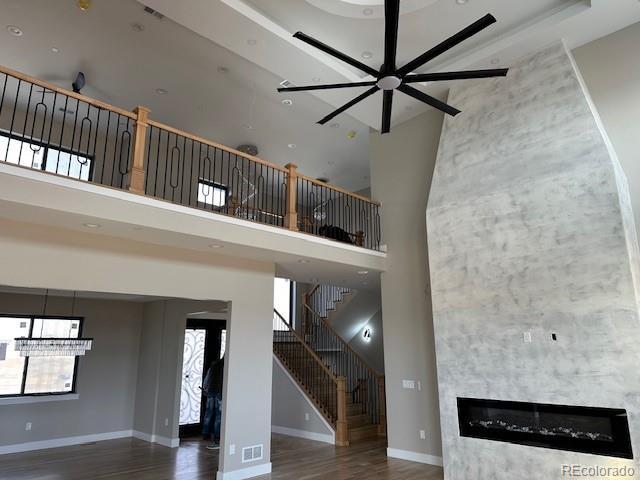 unfurnished living room featuring a towering ceiling, a glass covered fireplace, wood finished floors, baseboards, and stairs