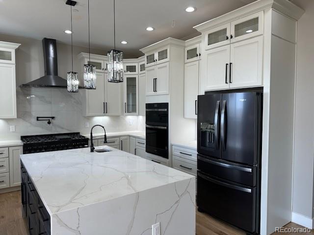 kitchen featuring black appliances, wall chimney range hood, white cabinets, and tasteful backsplash