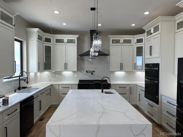 kitchen with dark wood-style floors, black appliances, a sink, and a center island with sink