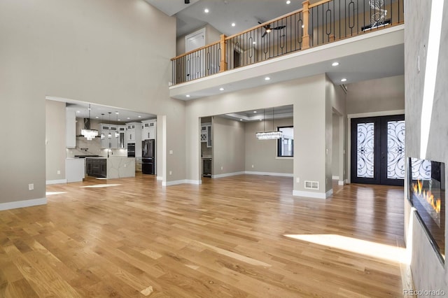 16250 Kenosha St, Brighton, CO 80603 - unfurnished living room featuring visible vents, baseboards, light wood-type flooring, french doors, and a high ceiling