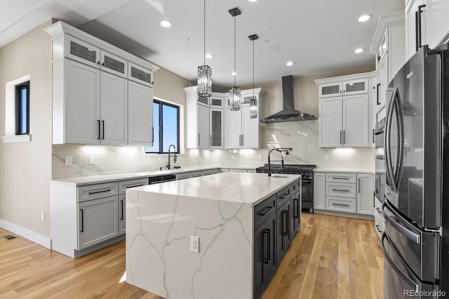 16250 Kenosha St, Brighton, CO 80603 - kitchen featuring wall chimney range hood, a center island with sink, range with gas stovetop, light wood-style flooring, and freestanding refrigerator