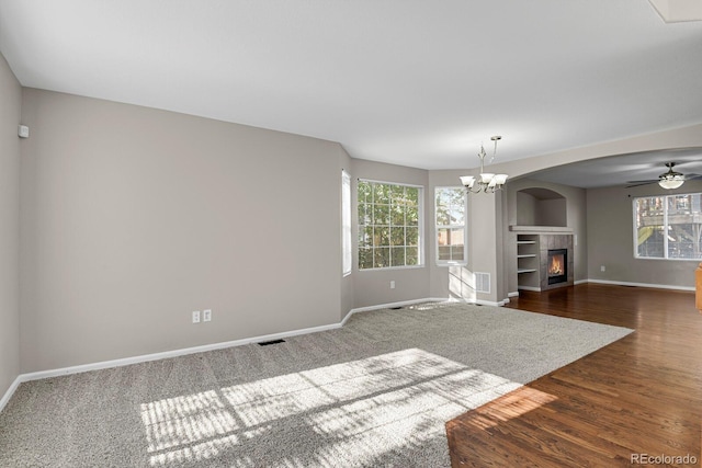 unfurnished living room featuring dark wood-type flooring, ceiling fan with notable chandelier, and a healthy amount of sunlight