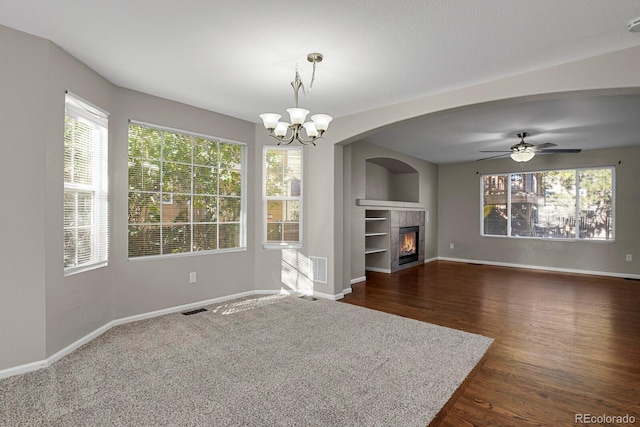 unfurnished living room featuring ceiling fan with notable chandelier, a tiled fireplace, dark hardwood / wood-style flooring, and a wealth of natural light