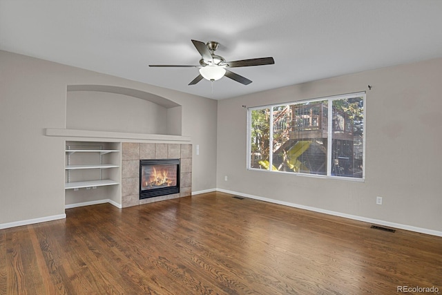 unfurnished living room featuring ceiling fan, a tiled fireplace, and hardwood / wood-style floors