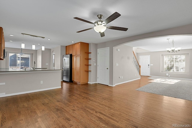 unfurnished living room with dark wood-type flooring, ceiling fan with notable chandelier, sink, and a healthy amount of sunlight