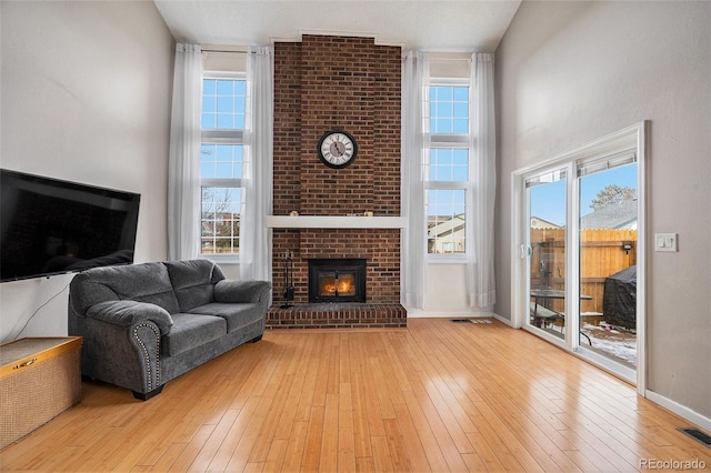 living room featuring wood-type flooring, a brick fireplace, and a healthy amount of sunlight