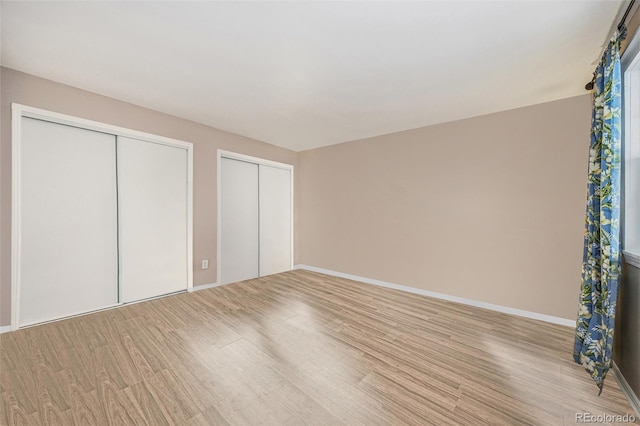 unfurnished bedroom featuring multiple closets and light hardwood / wood-style flooring