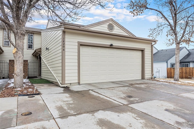 garage featuring concrete driveway and fence