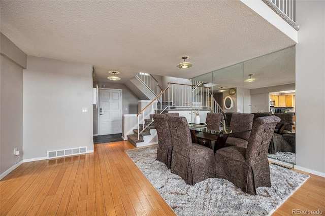 dining space with a textured ceiling, visible vents, baseboards, stairway, and wood-type flooring