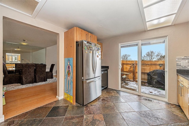 kitchen featuring baseboards, visible vents, dark countertops, freestanding refrigerator, and stone tile flooring