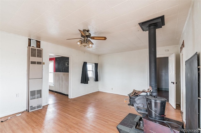 7080 S Calhan Rd, Calhan, CO 80808 - unfurnished living room featuring a wood stove, light wood finished floors, a ceiling fan, a heating unit, and baseboards
