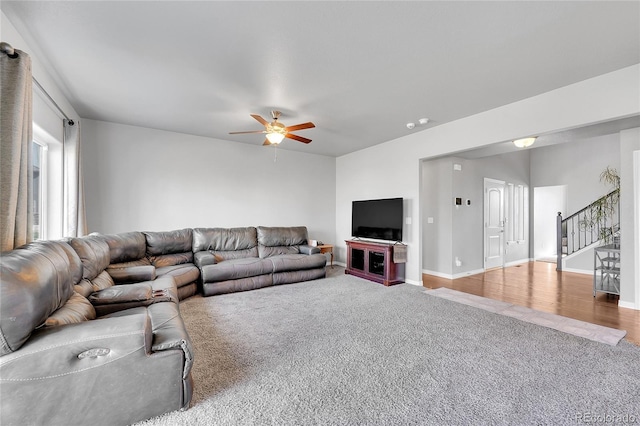 carpeted living area featuring baseboards, a ceiling fan, and stairway