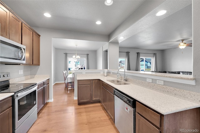 kitchen with light wood-style floors, ceiling fan with notable chandelier, recessed lighting, a sink, and stainless steel appliances