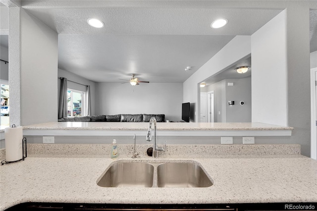 kitchen featuring open floor plan, light stone counters, ceiling fan, and a sink