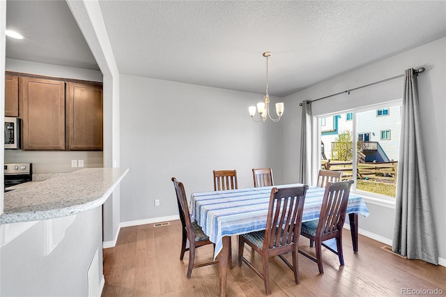 dining room with light wood finished floors, a notable chandelier, baseboards, and visible vents