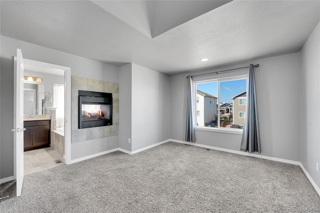 unfurnished living room with a textured ceiling, light colored carpet, baseboards, and a multi sided fireplace