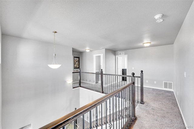 corridor with baseboards, an upstairs landing, a textured ceiling, carpet floors, and visible vents