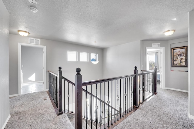 corridor featuring a textured ceiling, visible vents, carpet flooring, an upstairs landing, and baseboards