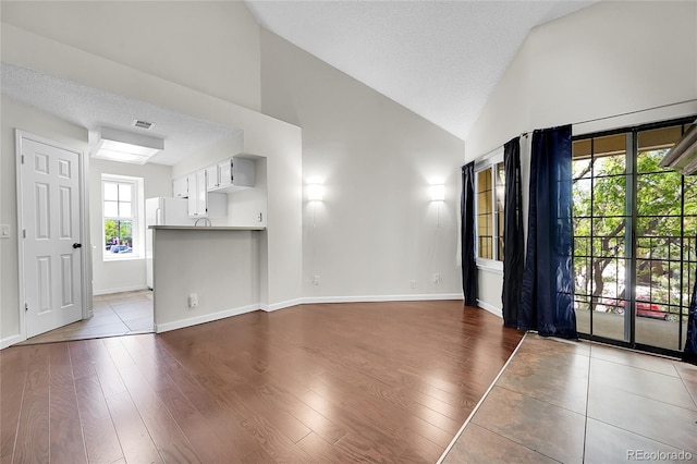 unfurnished living room featuring dark wood-type flooring, high vaulted ceiling, baseboards, and a textured ceiling
