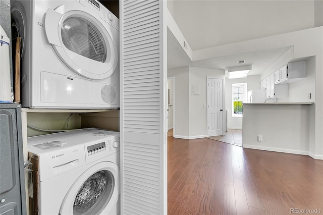 laundry area with stacked washer and clothes dryer, baseboards, and dark wood-type flooring