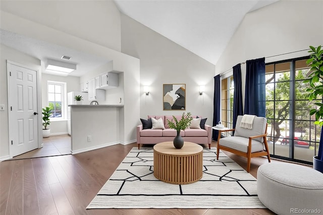 living area with high vaulted ceiling, wood finished floors, and baseboards