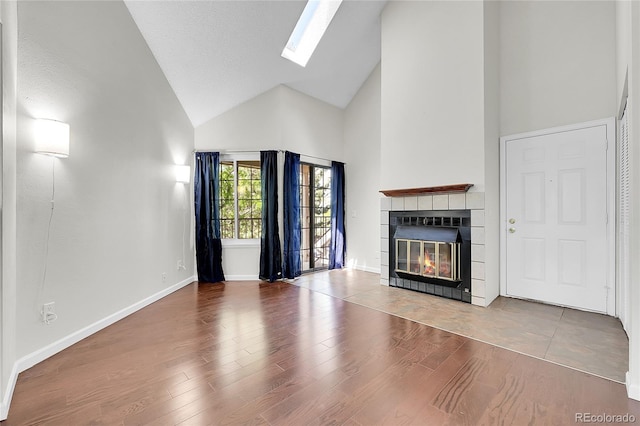 unfurnished living room featuring high vaulted ceiling, a tile fireplace, a skylight, wood finished floors, and baseboards