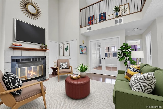 living area with french doors, a towering ceiling, a tile fireplace, and wood finished floors