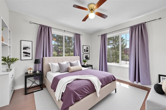 bedroom with multiple windows, wood finished floors, baseboards, ceiling fan, and a textured ceiling