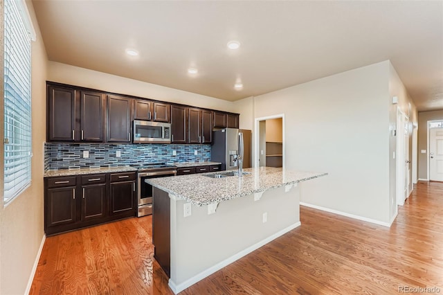 5841 Echo Park Cir, Castle Rock, CO 80104 - kitchen with appliances with stainless steel finishes, a center island with sink, dark brown cabinets, light wood finished floors, and backsplash