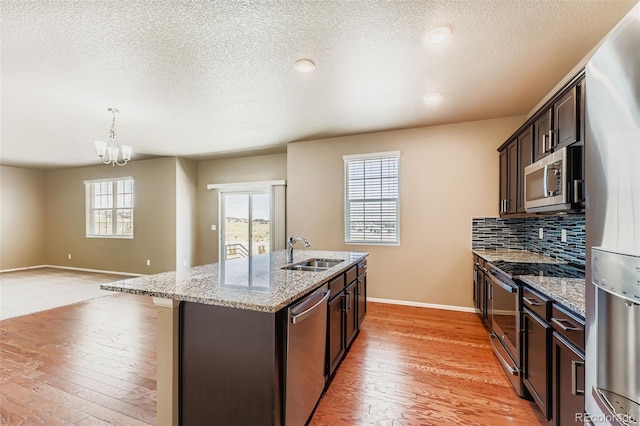 5841 Echo Park Cir, Castle Rock, CO 80104 - kitchen with stainless steel appliances, an island with sink, a textured ceiling, dark brown cabinets, and light wood-style floors