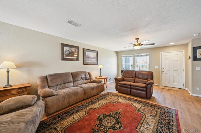living room with visible vents, baseboards, light wood-type flooring, a ceiling fan, and a textured ceiling