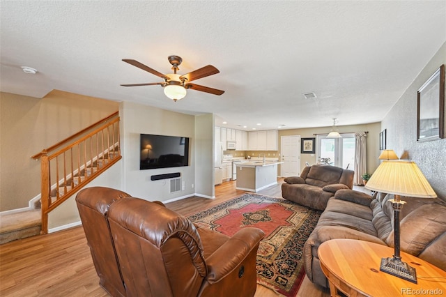 living room with stairs, light wood-style floors, baseboards, and a ceiling fan