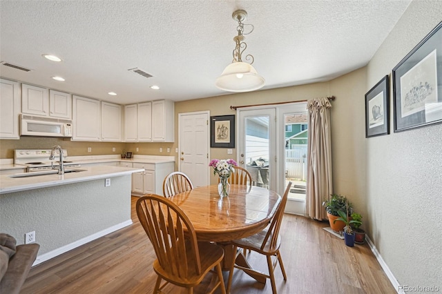 dining area featuring visible vents, light wood-type flooring, and a textured ceiling