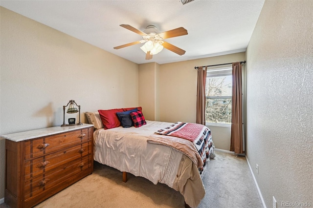 bedroom with ceiling fan, light colored carpet, and a textured wall