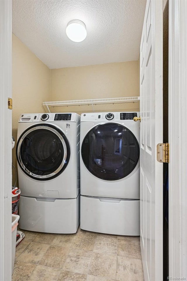 washroom with laundry area, washing machine and clothes dryer, and a textured ceiling