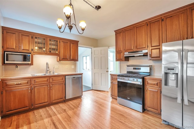 kitchen featuring appliances with stainless steel finishes, under cabinet range hood, a sink, brown cabinetry, and light countertops
