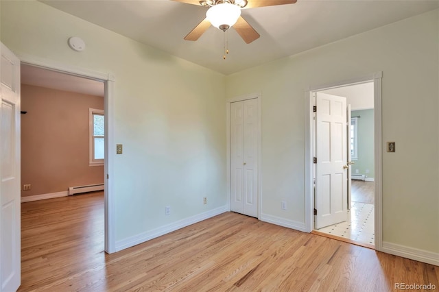 unfurnished bedroom with a baseboard heating unit, light wood-style floors, baseboards, and a closet