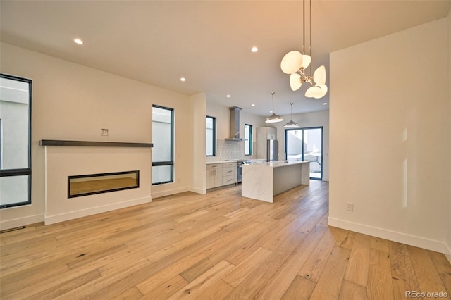 kitchen with a kitchen island with sink, hanging light fixtures, light hardwood / wood-style flooring, wall chimney exhaust hood, and tasteful backsplash