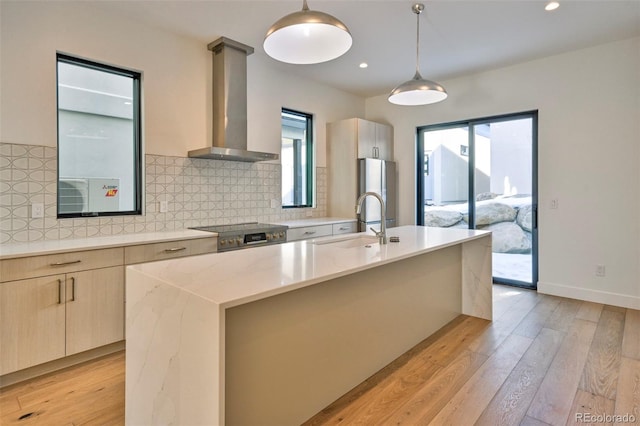 kitchen with a wealth of natural light, an island with sink, decorative light fixtures, and wall chimney range hood