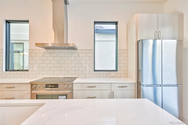 kitchen with wall chimney exhaust hood, light stone countertops, decorative backsplash, and stainless steel appliances