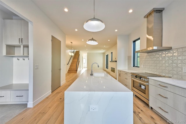 kitchen with light stone counters, wall chimney exhaust hood, decorative light fixtures, high end stainless steel range, and a large island