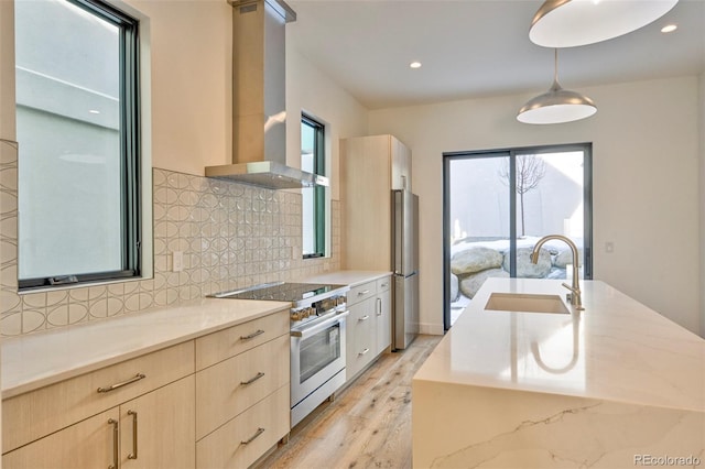 kitchen with appliances with stainless steel finishes, light wood-type flooring, wall chimney exhaust hood, sink, and hanging light fixtures