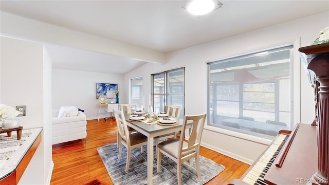 dining room with wood-type flooring, lofted ceiling with beams, and a wealth of natural light