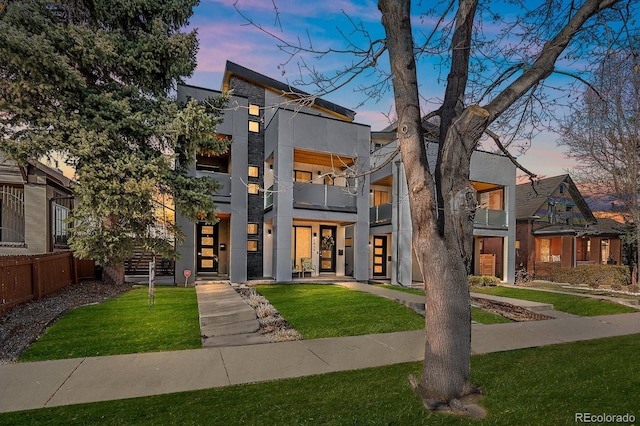 contemporary house with a yard, fence, and stucco siding