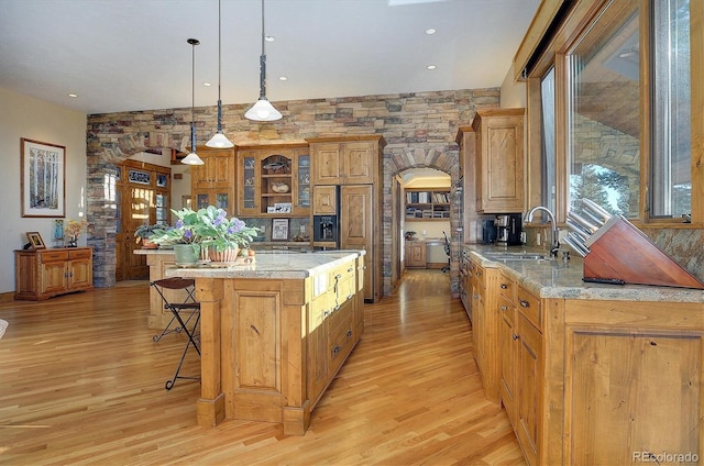 kitchen with sink, decorative light fixtures, a kitchen breakfast bar, a kitchen island, and light stone countertops