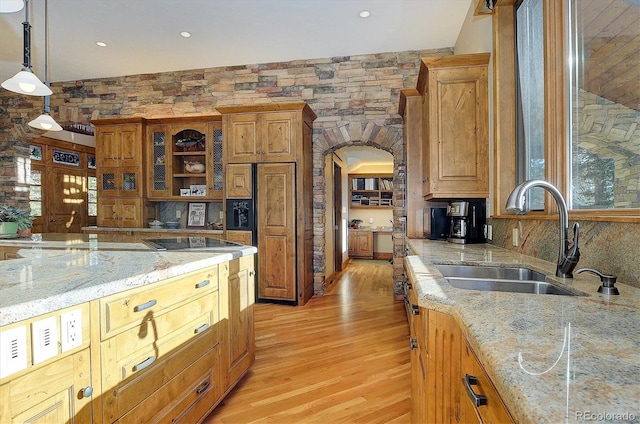 kitchen with decorative light fixtures, sink, light stone counters, paneled refrigerator, and light hardwood / wood-style flooring