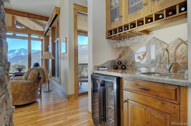 bar featuring plenty of natural light, sink, beverage cooler, a mountain view, and light stone countertops