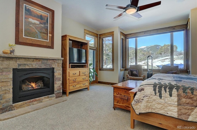 bedroom with a stone fireplace, carpet floors, and ceiling fan