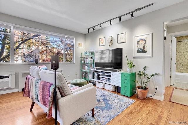 living room featuring wood-type flooring, rail lighting, a wall mounted AC, and radiator heating unit